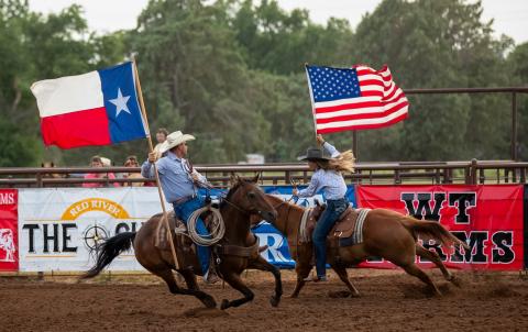 Rodeo fans rise to their feet as the father-daughter duo of Todd and Ellie Thomas carry the colors in the July 1, 2022, performance of the Wellington Fourth of July Rodeo. Witness the 2025 event scheduled for Thursday, July 3-Saturday, July 5 at the Wellington Fairgrounds. HZW Media