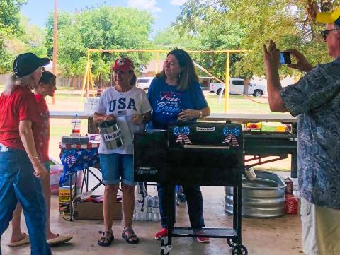 Sheltered from the sun beneath the Ellison Park pavilion, Barbara Duncan, left, claims the 20-inch pellet grill, donated by Bawcom Supply, as Evelyn Henard, second from left, drew her name at the Saturday, June 22 “Party in the Park” fundraiser event at Ellison Park. Organizers Karen Caldwell and Margret Wood witnessed the drawing as Neal Odom, right, provided the Facebook live feed. The Red River Sun/Bev Odom